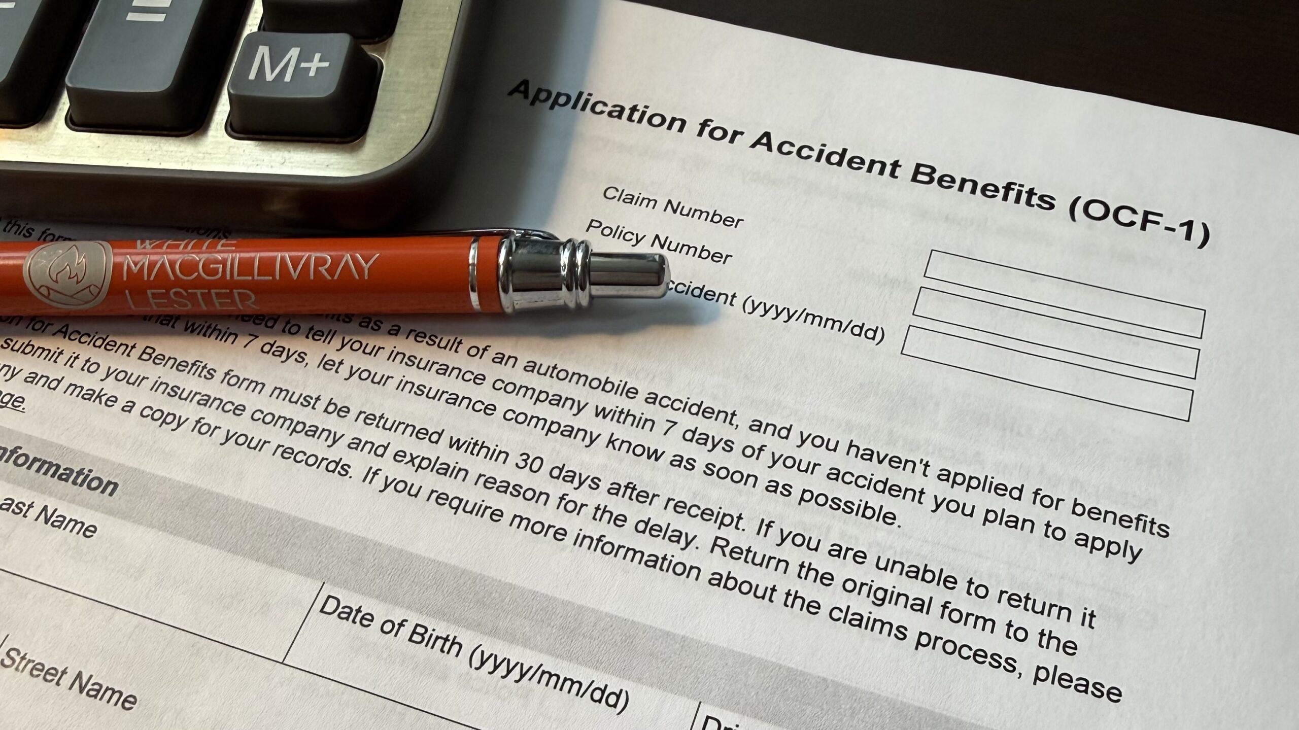 Blank Ontario OCF-1 Application for Accident Benefits form on a desk with a calculator and a White Macgillivray Lester pen.