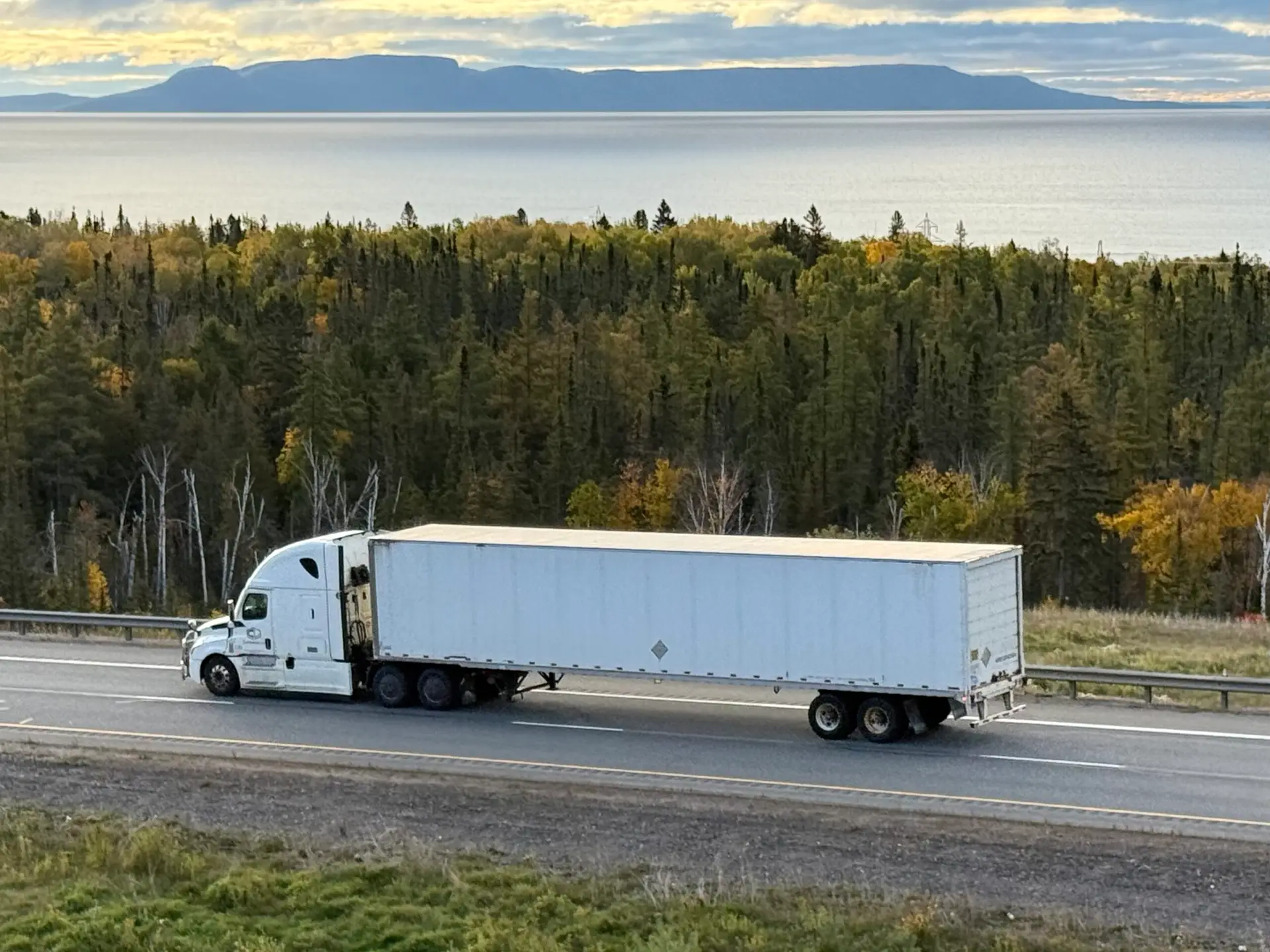 White tractor-trailer on Highway 11/17 near Thunder Bay, with Lake Superior and the Sleeping Giant in the background.